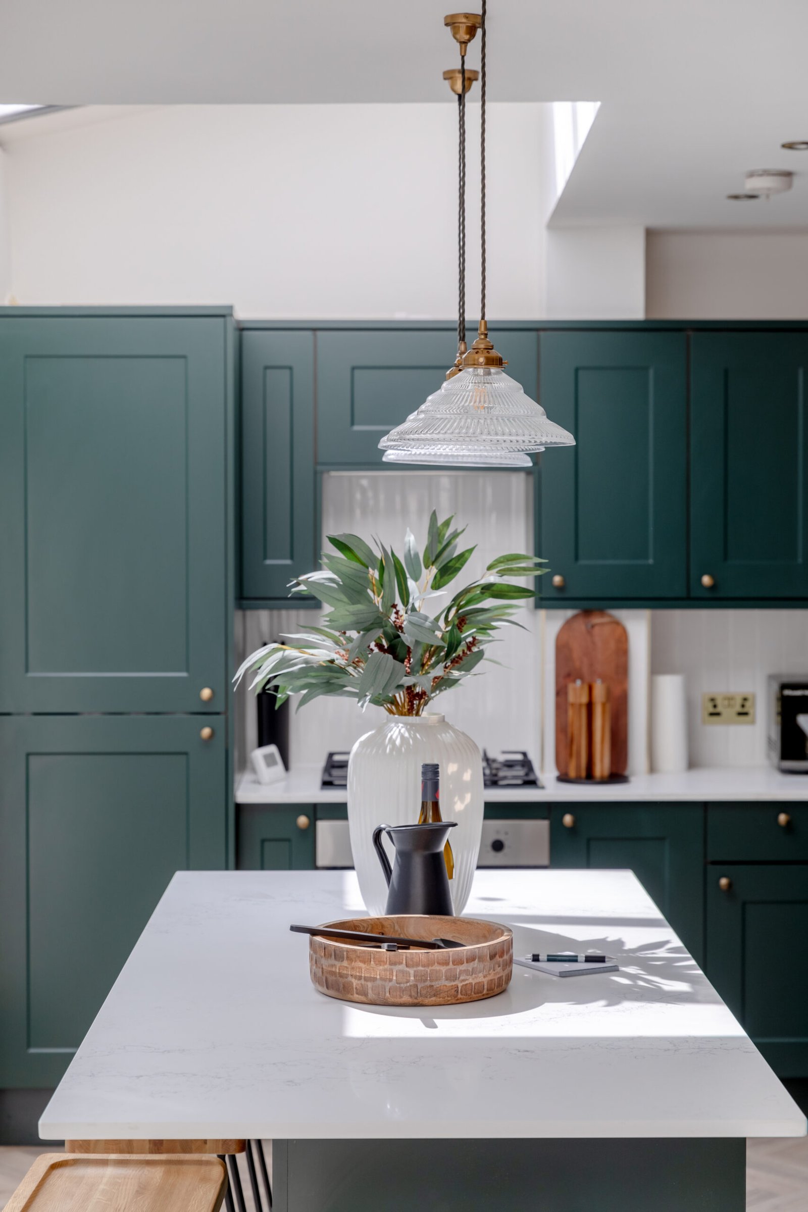 A modern kitchen with dark green cupboard doors, white marble countertops, nicely decorated for property photography.