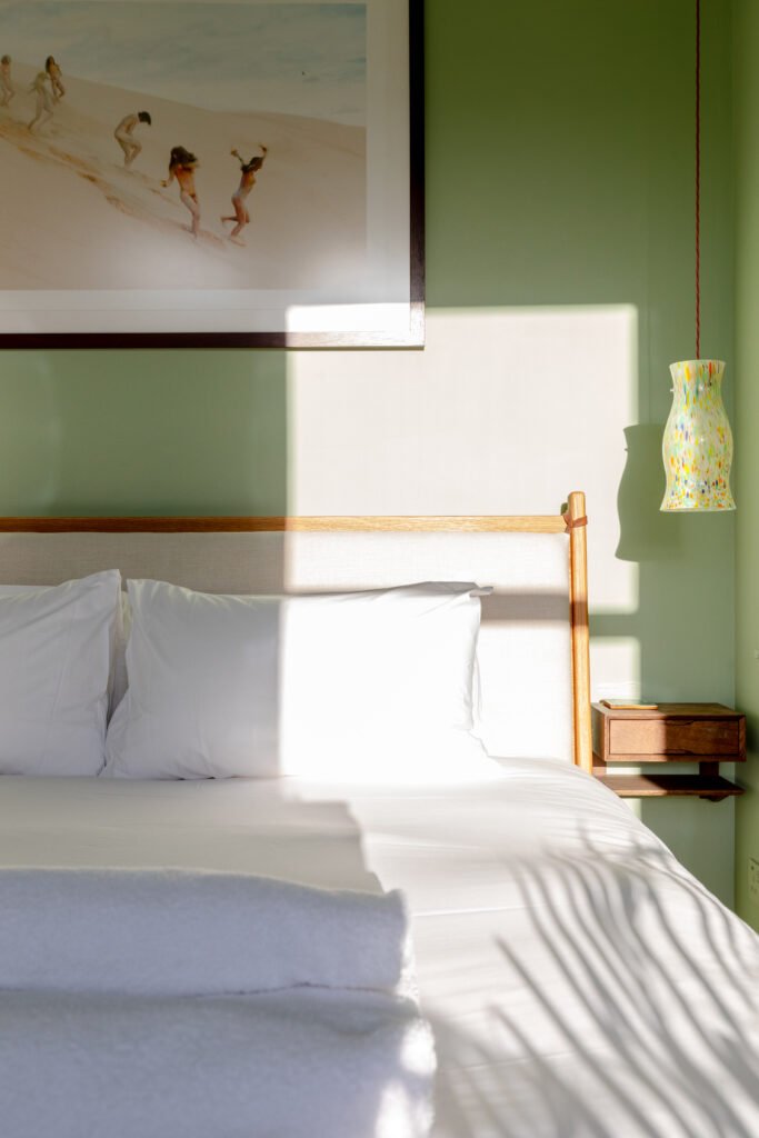 Close up shoot of a double bed with white sheets, green wall.