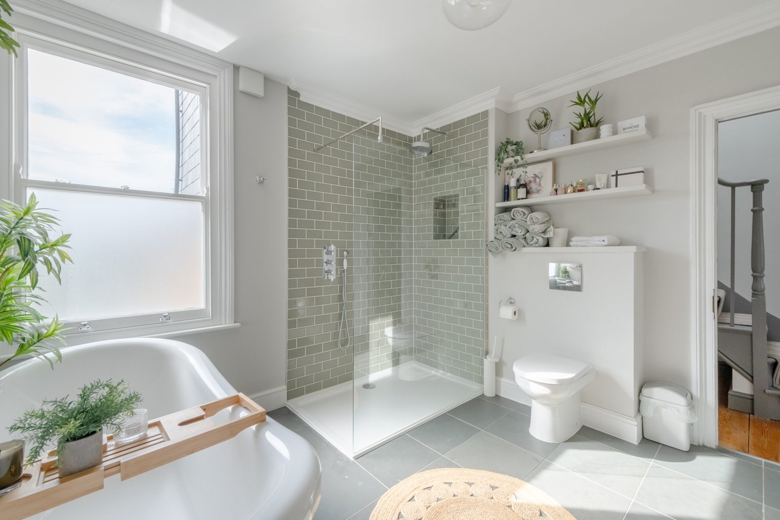 Modern designed bathroom with a bath tub, shower, toilet, light green soft coloured, taken for Airbnb photography.