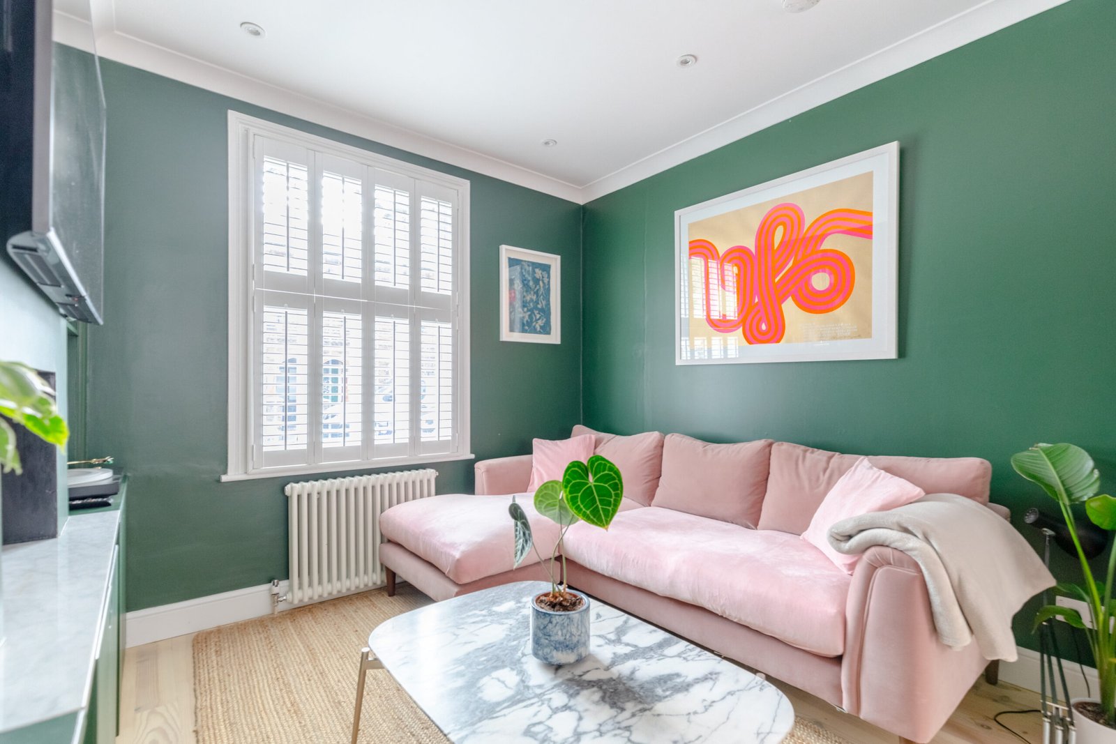 A living room with a 3 seat, pink sofa, dark green walls, from an Airbnb house, a marble coffee table in the centre.