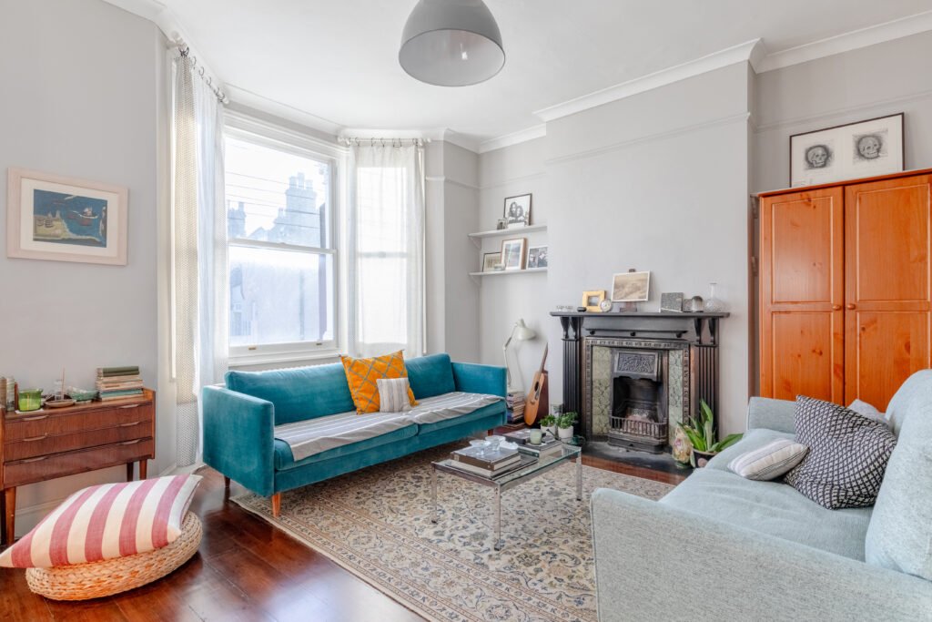 A warm designed living room with a turquoise sofa, a fireplace, wooden floor and a classic pattern carpet.