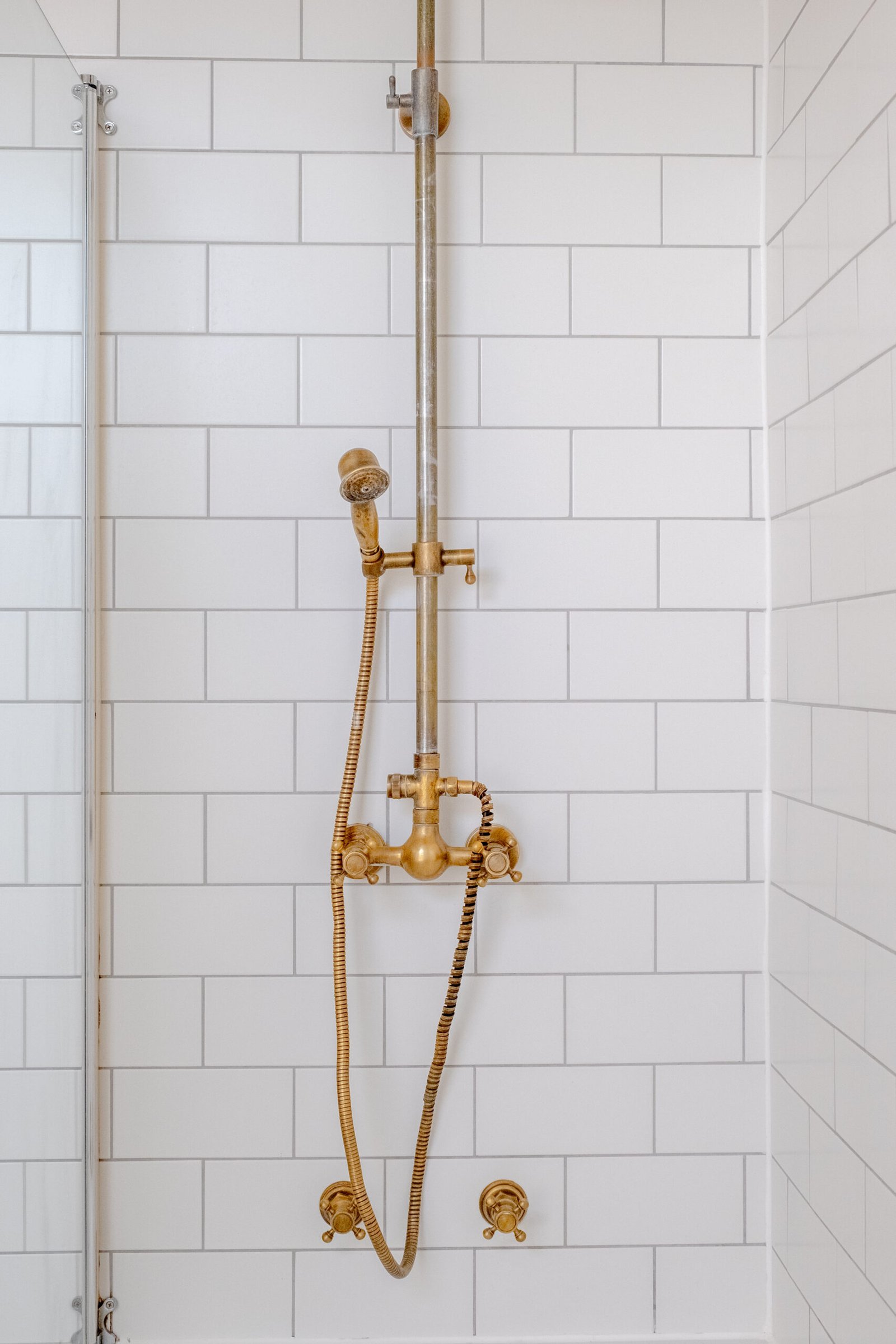 A detail photo from an Airbnb house bathroom, capturing white tiled shower with bronze fixtures.