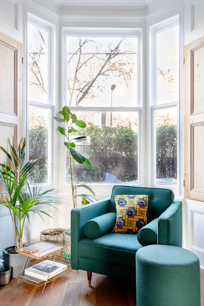A green armchair in front of the window in the living room of an Airbnb house.