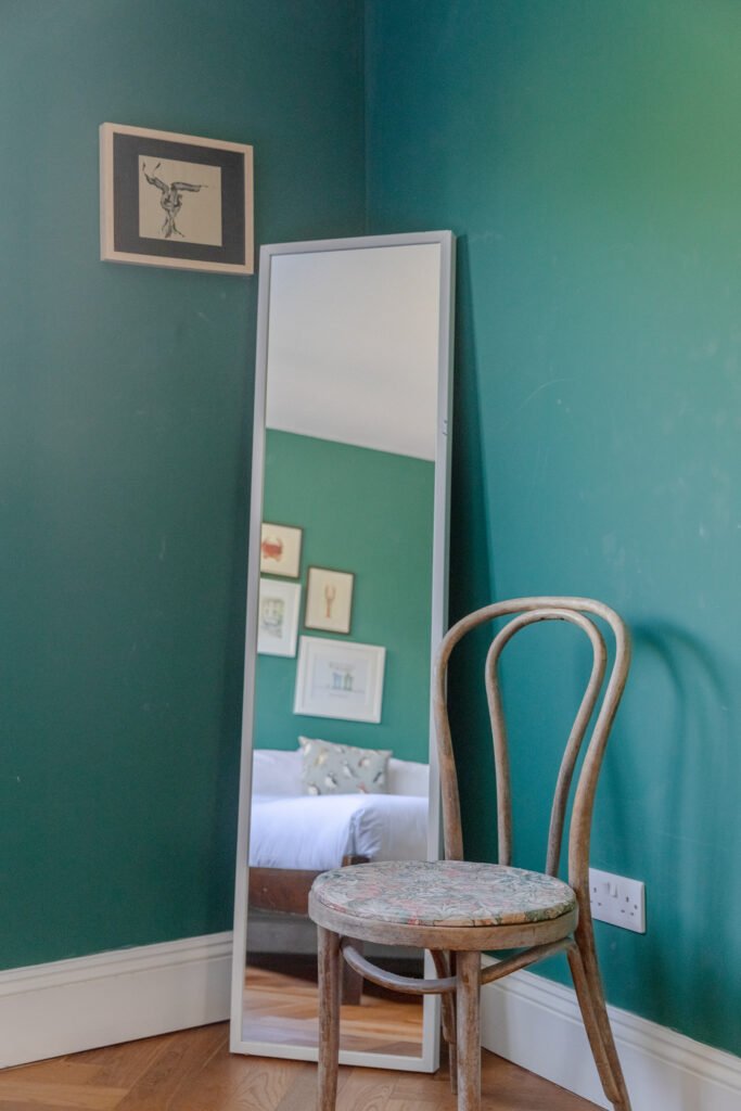 A chair at the corner of a room in a house, with dark green walls, taken for Airbnb photography.