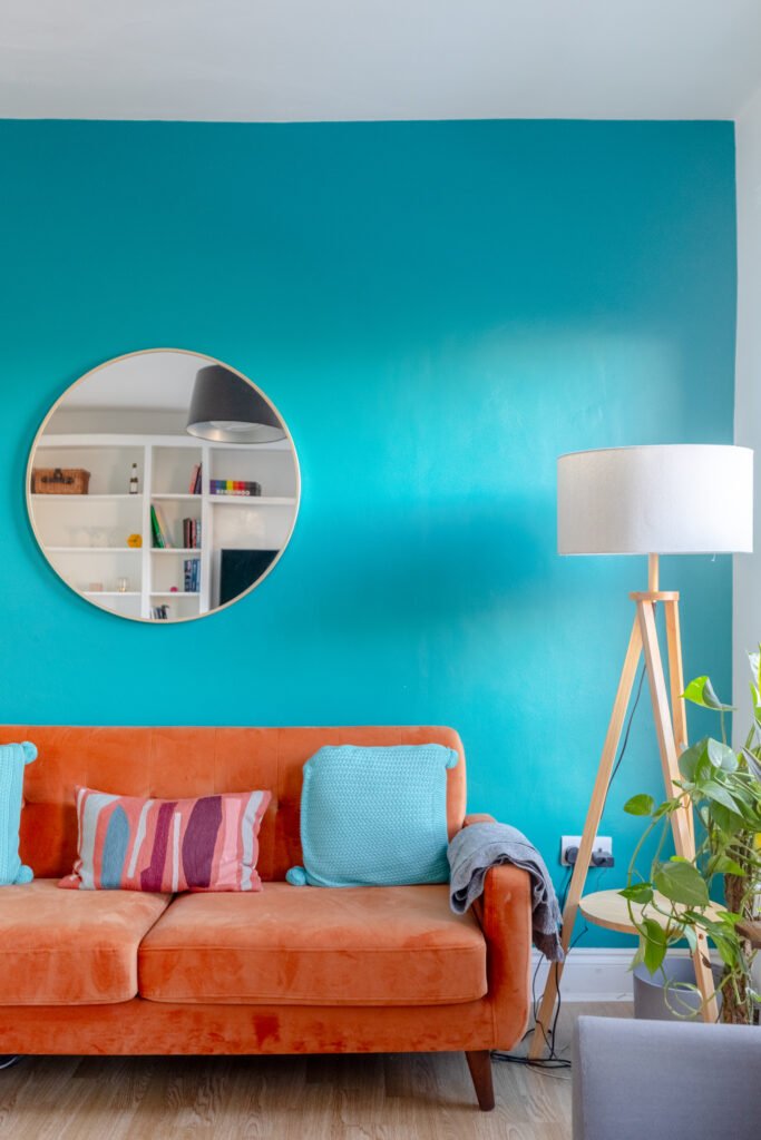 A turquoise wall with a coral sofa in front of it