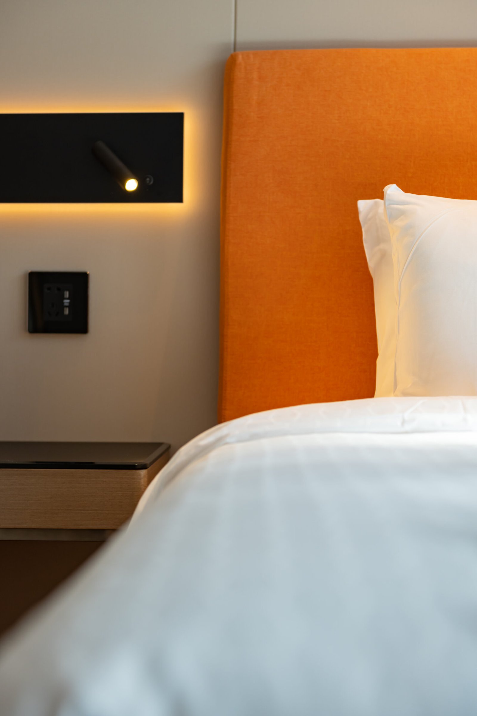 Partial image of a bed in a hotel room, with an orange headboard, vertical image.